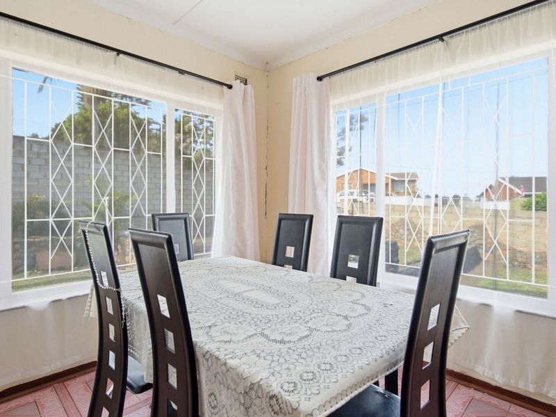 A bright dining area featuring large windows with security bars and tiled flooring, offering a view of the exterior garden space.