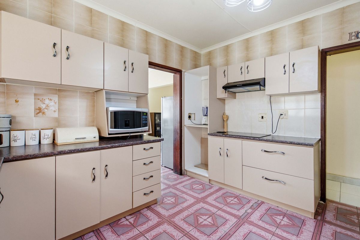 A functional kitchen featuring built-in cabinetry, laminate countertops, an electric hob with extractor fan, and tiled finishes throughout.