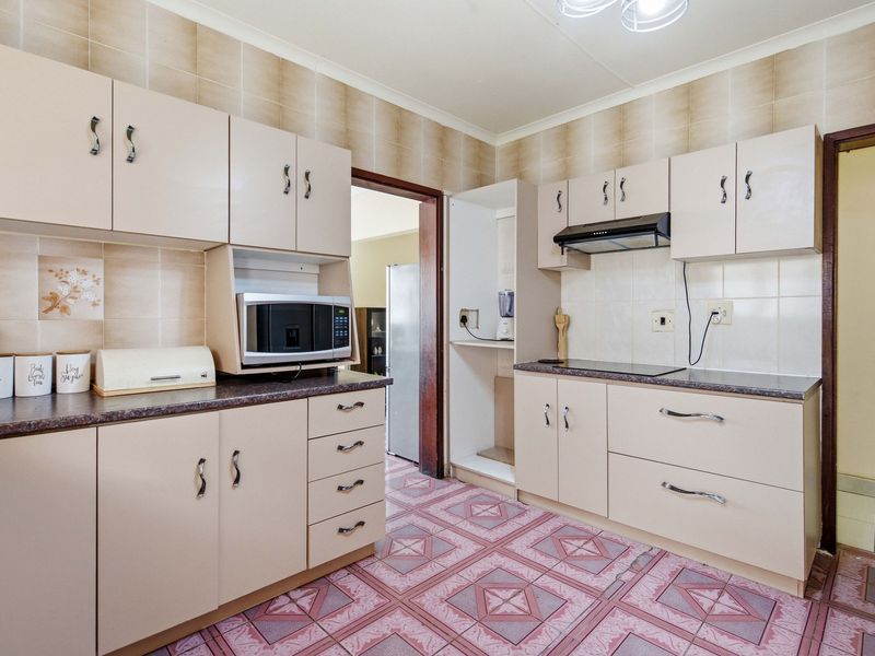 A functional kitchen featuring built-in cabinetry, laminate countertops, an electric hob with extractor fan, and tiled finishes throughout.