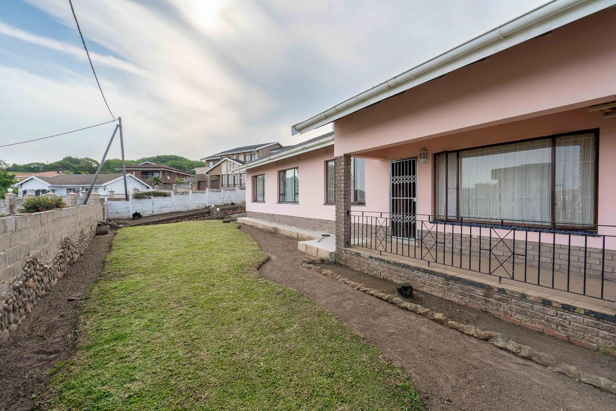 Rear view of the property featuring a covered patio with metal security gate, brick boundary wall, and a lawn area requiring further landscaping.