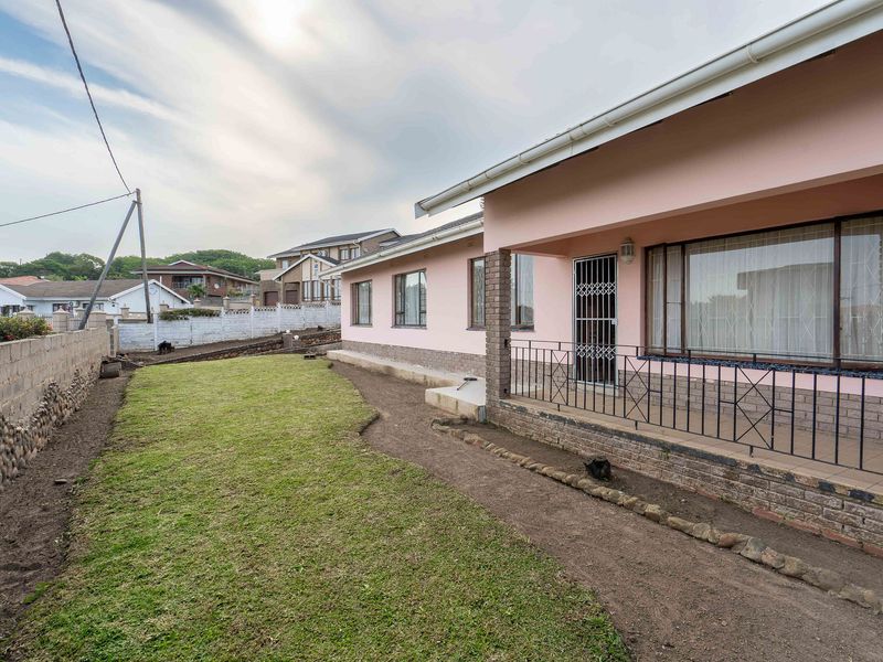 Rear view of the property featuring a covered patio with metal security gate, brick boundary wall, and a lawn area requiring further landscaping.