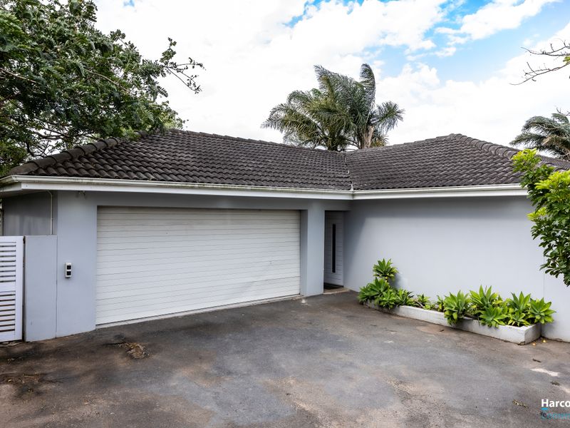 Front exterior view of the property featuring a double garage with a tiled roof, asphalt driveway, and a built-in concrete planter.
