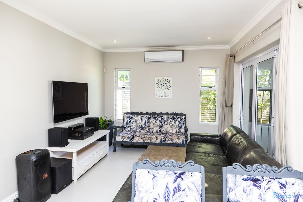 A well-maintained living room featuring tiled flooring, a split-system air conditioner, and large aluminium sliding doors providing access to the outdoor area.