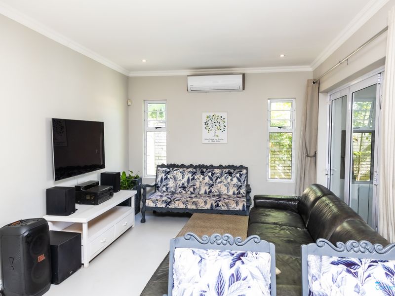 A well-maintained living room featuring tiled flooring, a split-system air conditioner, and large aluminium sliding doors providing access to the outdoor area.
