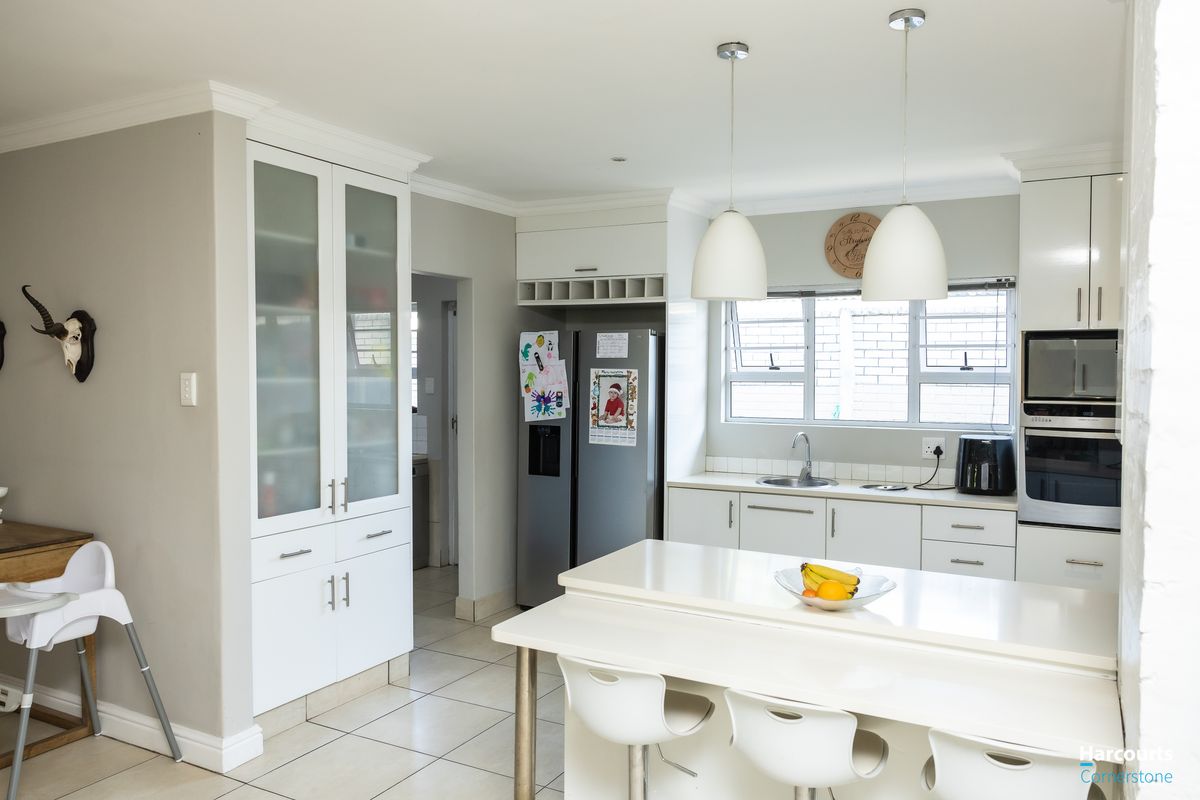 Modern kitchen featuring white cabinetry, a central island with breakfast bar seating, built-in appliances, and tiled flooring, offering a clean and functional workspace.