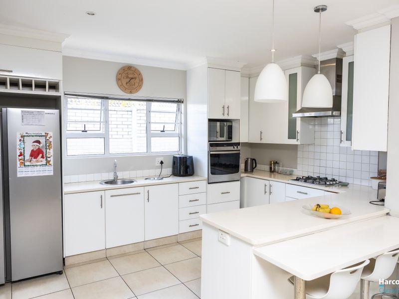 Modern kitchen featuring white cabinetry, stone countertops, built-in appliances, gas hob, and tiled flooring with a functional breakfast bar layout.