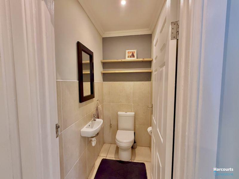 A compact guest bathroom featuring a wall-mounted basin, toilet, neutral wall tiling, and floating wooden shelves.