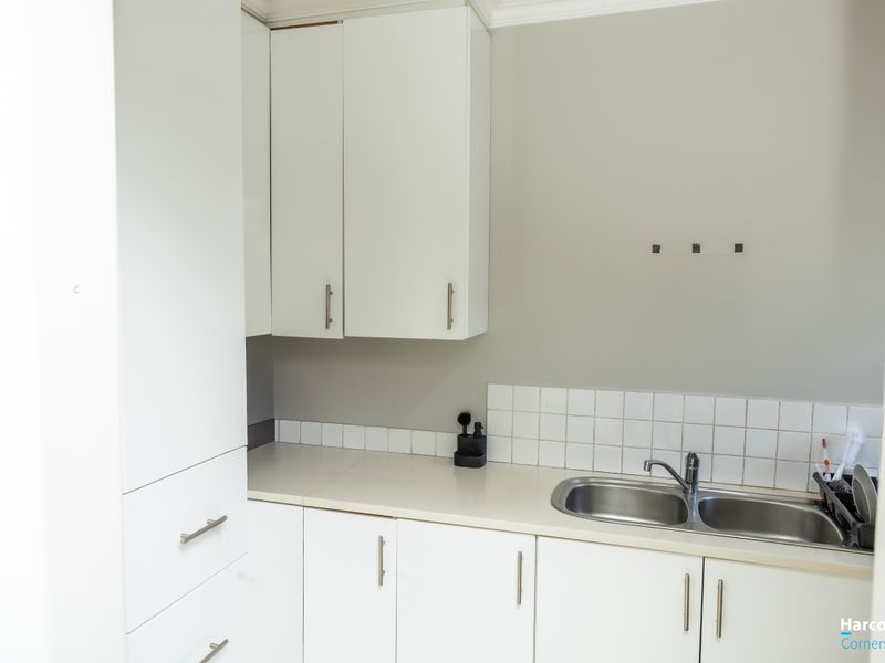 A clean and functional laundry area featuring white built-in cabinetry, a double stainless steel sink with a mixer tap, and a tiled splashback.
