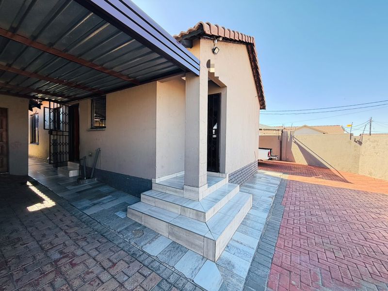 Front exterior view featuring a covered carport, tiled entrance steps, and a paved driveway with secure perimeter walling.