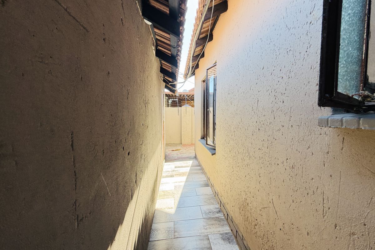 A narrow side passage or exterior walkway featuring tiled flooring and textured wall finishes between two building structures.