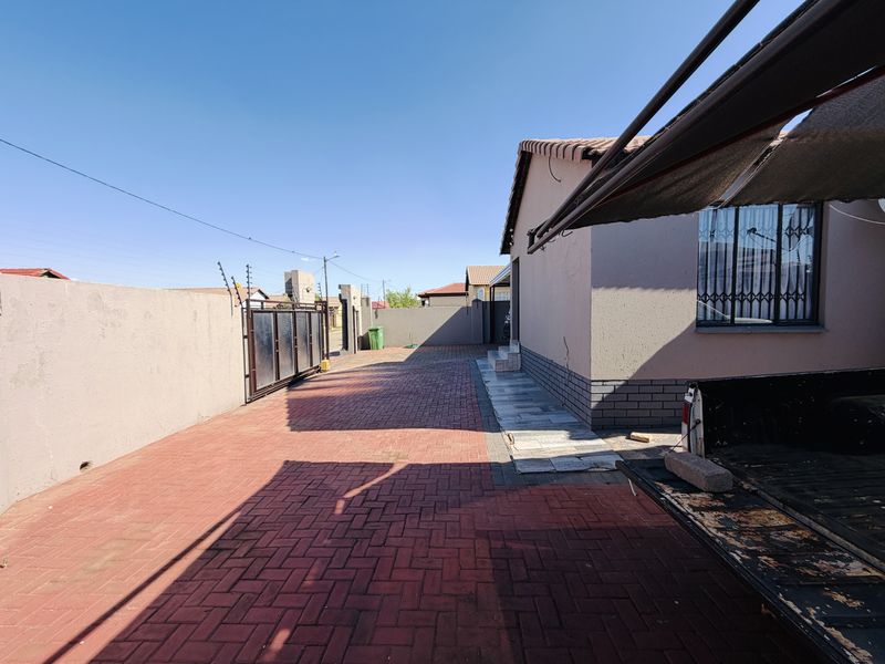 Exterior view of the property featuring a paved driveway, perimeter wall with electric fencing, and secure gated access.