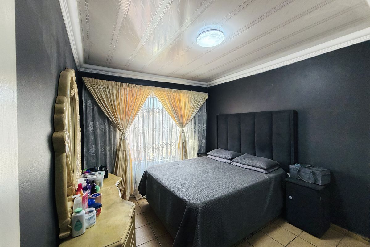 A bedroom featuring tiled flooring, decorative ceiling panels, and crown molding, providing a functional space with dark wall finishes.