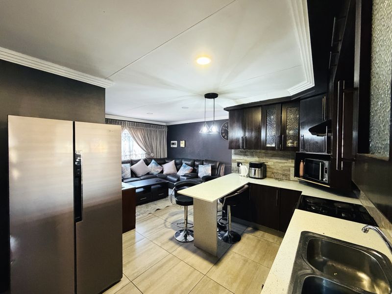 Open-plan kitchen and living area featuring dark wood cabinetry, stone countertops, a breakfast bar, and tiled flooring throughout.