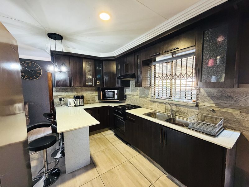 Modern kitchen featuring dark wood cabinetry, stone countertops, a breakfast bar, and integrated appliances with tiled flooring and contemporary finishes.