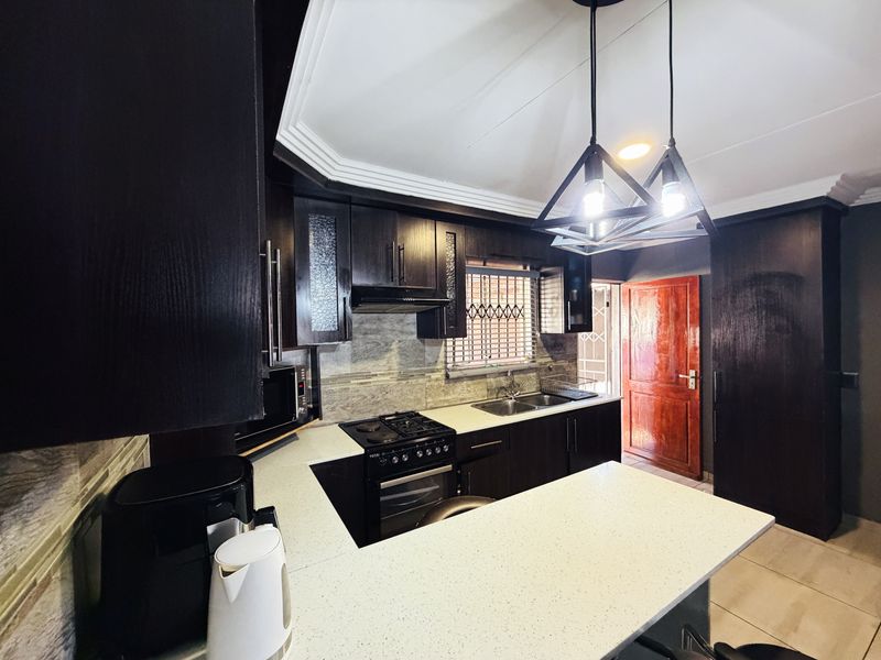 Modern kitchen featuring dark wood cabinetry, stone countertops, built-in oven, gas hob, and stylish pendant lighting, offering a functional and contemporary cooking space.