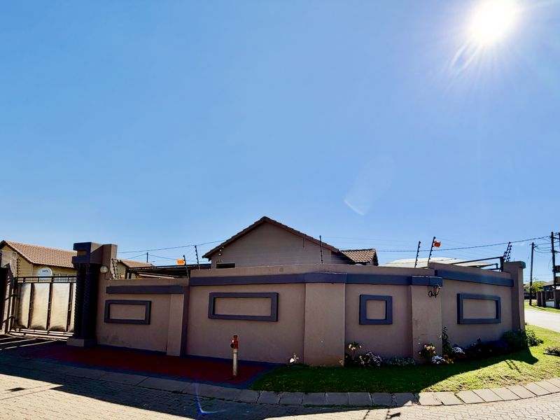 Front exterior view of the property featuring a secure perimeter wall with electric fencing, a sliding gate, and a paved driveway.