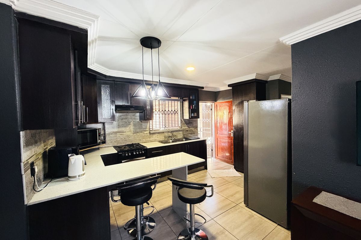 Modern kitchen featuring dark wood cabinetry, stone countertops, gas hob, extractor fan, and tiled flooring with a breakfast bar area.