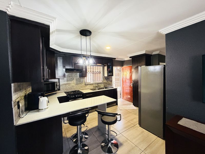 Modern kitchen featuring dark wood cabinetry, stone countertops, gas hob, extractor fan, and tiled flooring with a breakfast bar area.