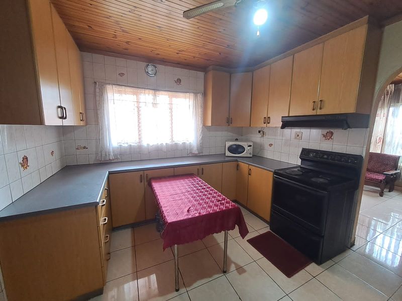 A functional kitchen featuring timber ceilings, laminate cabinetry, tiled backsplash, and tiled flooring, offering a classic layout with potential for modern updates.