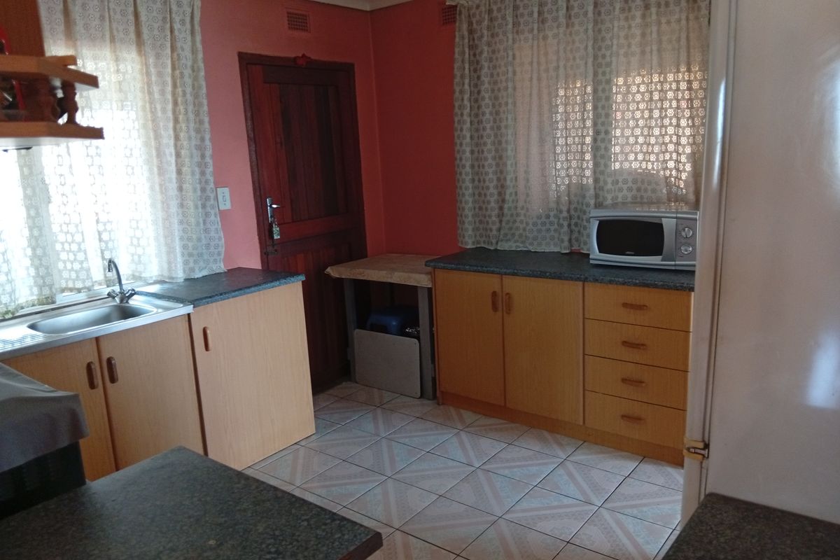 A functional kitchen featuring laminate cabinetry, tiled flooring, and a stainless steel sink, offering a dated aesthetic ready for modern updates.