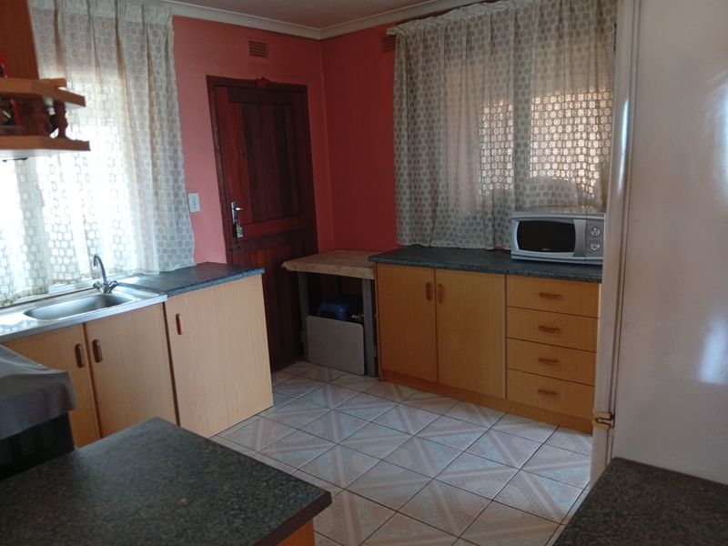 A functional kitchen featuring laminate cabinetry, tiled flooring, and a stainless steel sink, offering a dated aesthetic ready for modern updates.