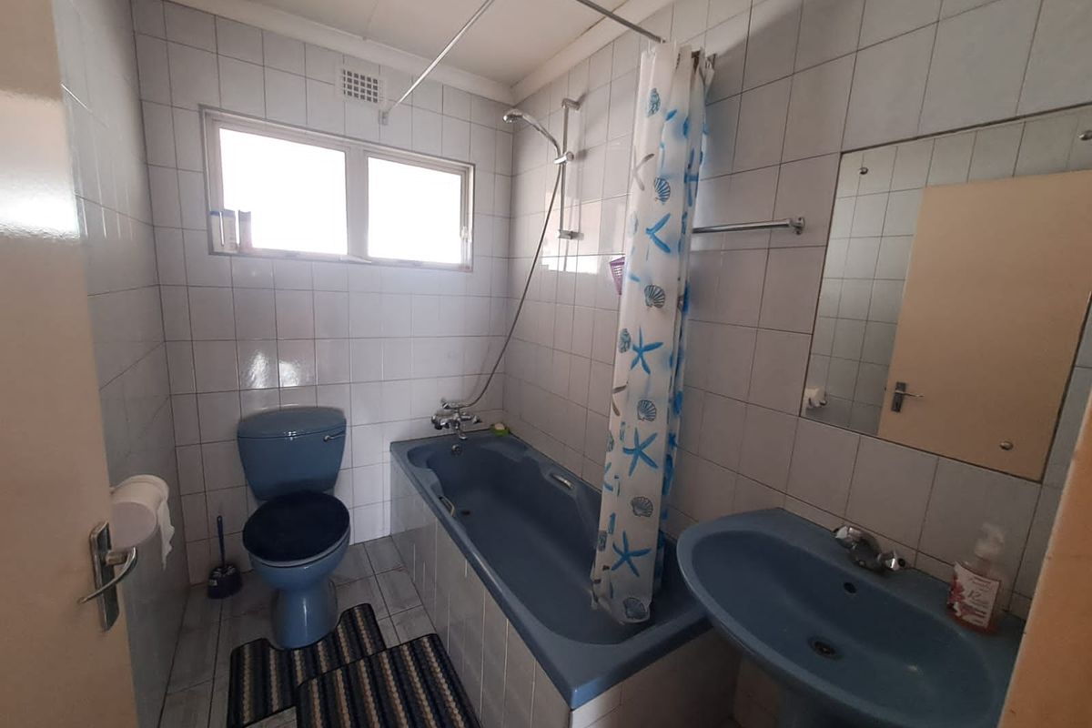 A functional bathroom featuring dated blue sanitaryware, a combined shower and bathtub, tiled walls, and a wall-mounted mirror.