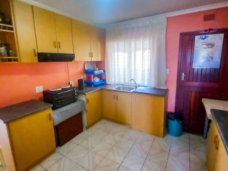 A functional kitchen featuring laminate cabinetry, tiled flooring, and a stainless steel sink, offering potential for modernization and aesthetic updates.