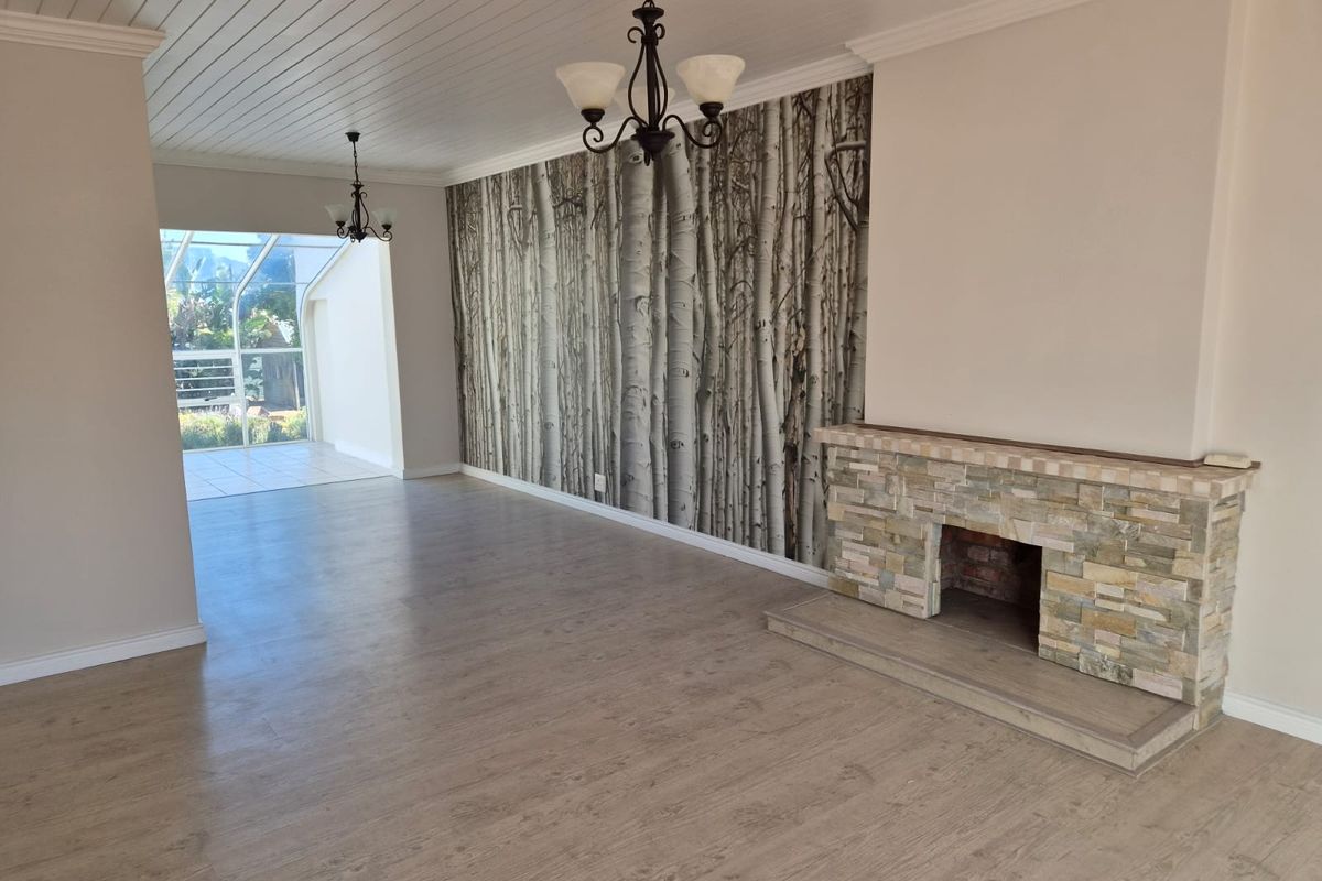 Spacious living room featuring a stone fireplace, wood-look laminate flooring, and a unique feature wall, leading to an enclosed patio area.