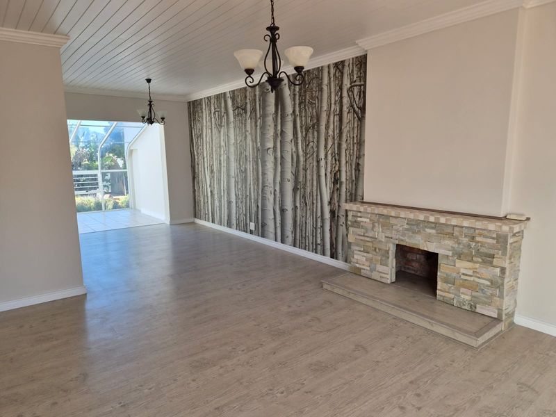 Spacious living room featuring a stone fireplace, wood-look laminate flooring, and a unique feature wall, leading to an enclosed patio area.
