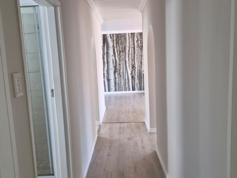 A bright, clean hallway featuring light wood-look laminate flooring, a white timber tongue and groove ceiling, and elegant archways leading to adjacent rooms.