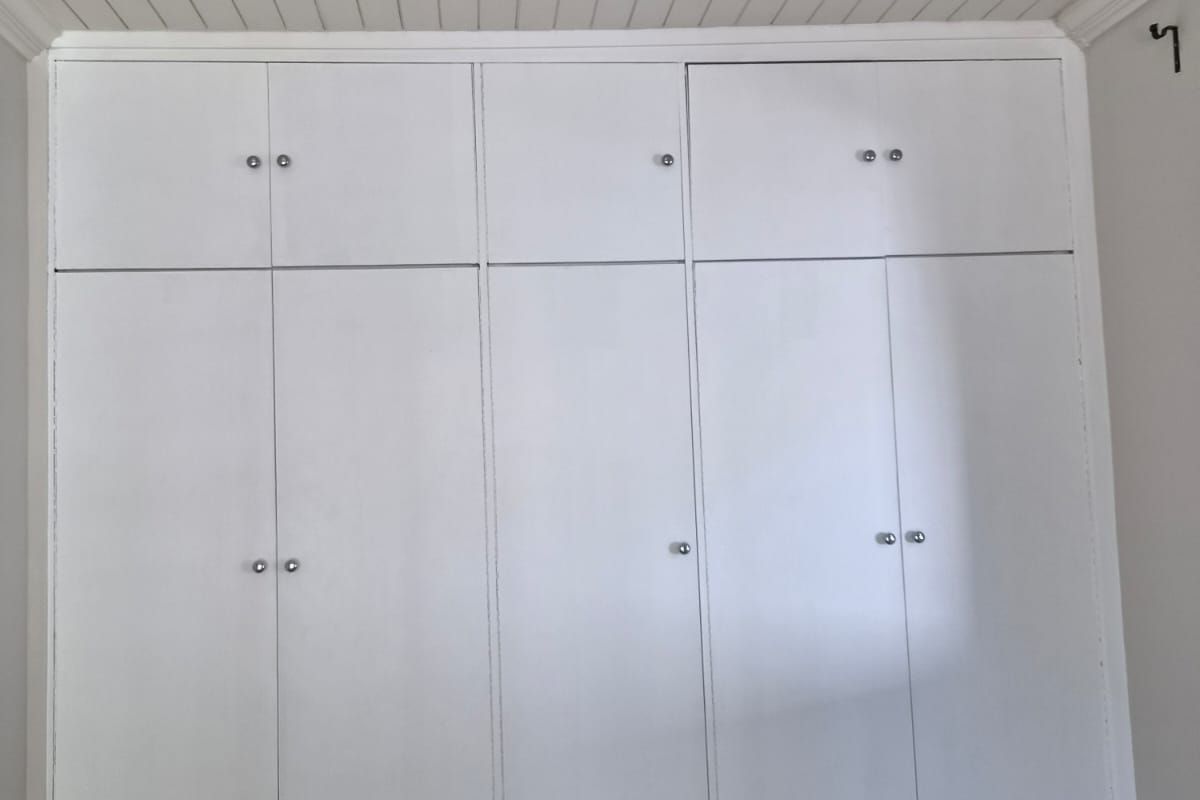 A clean bedroom featuring floor-to-ceiling white built-in cupboards and a classic tongue and groove ceiling.