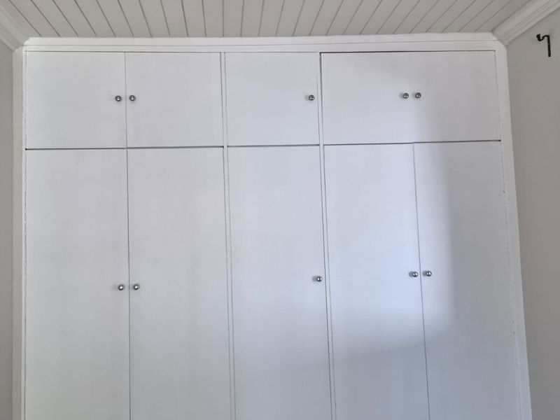 A clean bedroom featuring floor-to-ceiling white built-in cupboards and a classic tongue and groove ceiling.