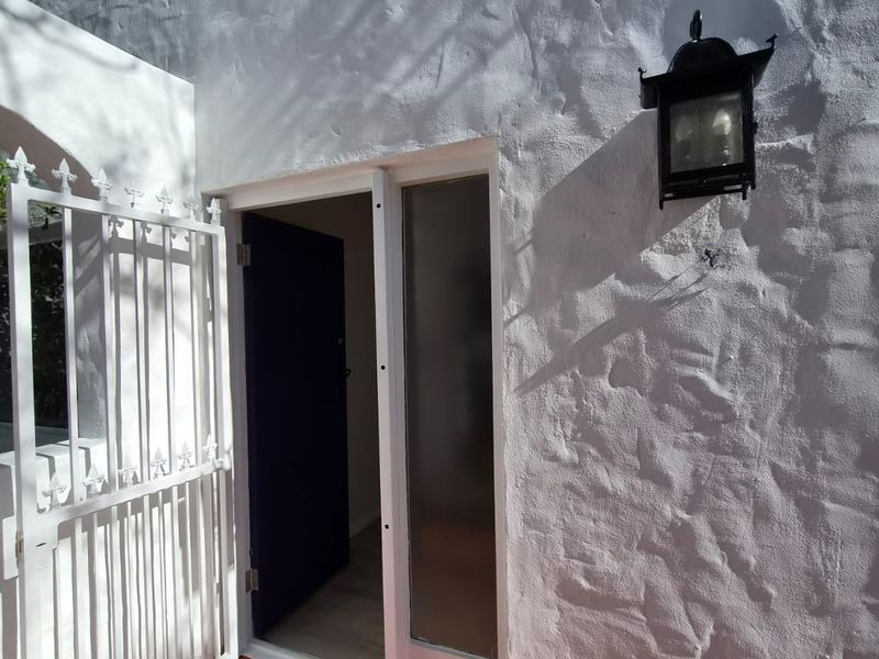 A bright entrance area featuring a textured white stucco facade, terracotta tiled flooring, a secure wrought iron gate, and a classic exterior wall lantern.