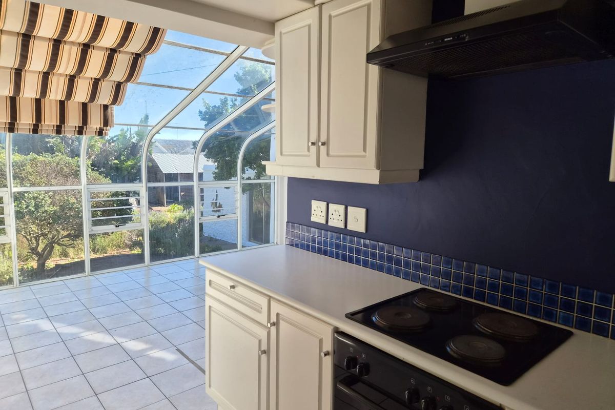A bright kitchen featuring built-in cabinetry, an electric hob, and an extractor fan, seamlessly connected to a sun-filled glass conservatory area.