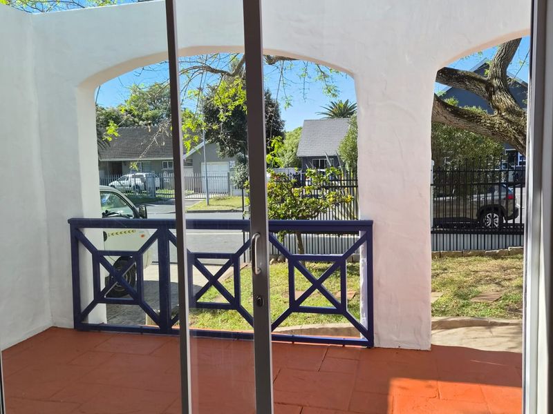 A covered patio area featuring terracotta tiling, arched masonry supports, and a decorative metal railing, viewed through a sliding glass door.