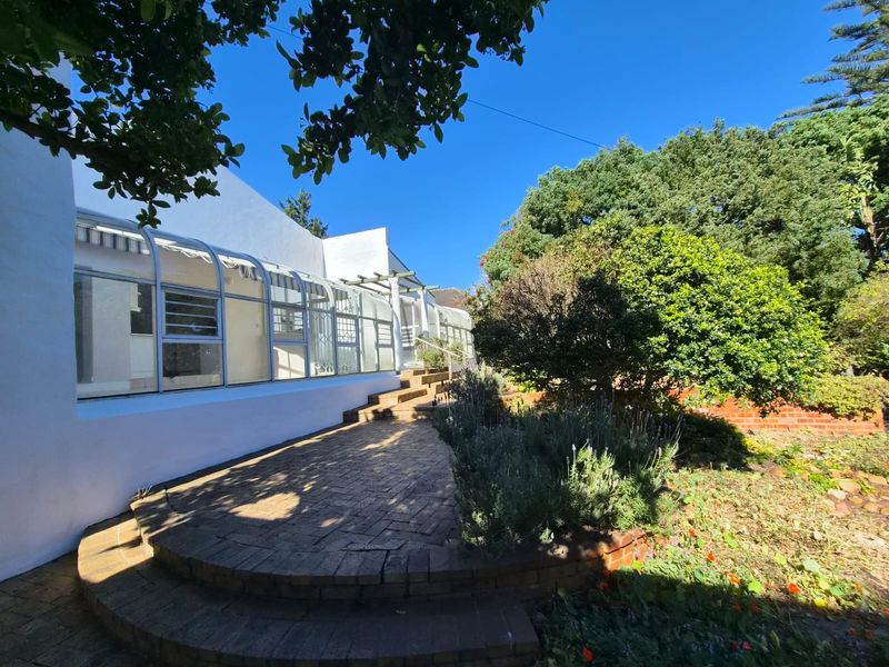 A well-maintained rear garden featuring a brick-paved patio area and a glass-enclosed sunroom extension with white exterior walls.