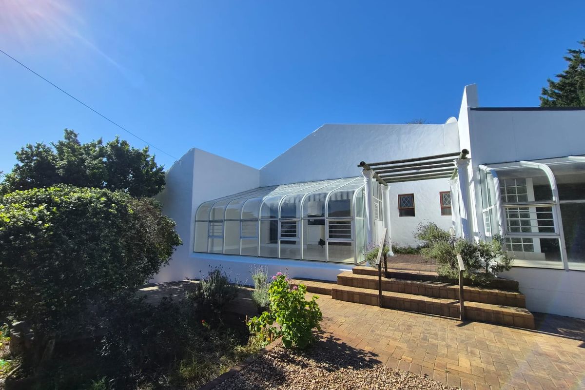 Rear view of the property featuring a glass conservatory, brick paved patio area, and a timber pergola leading to the garden.