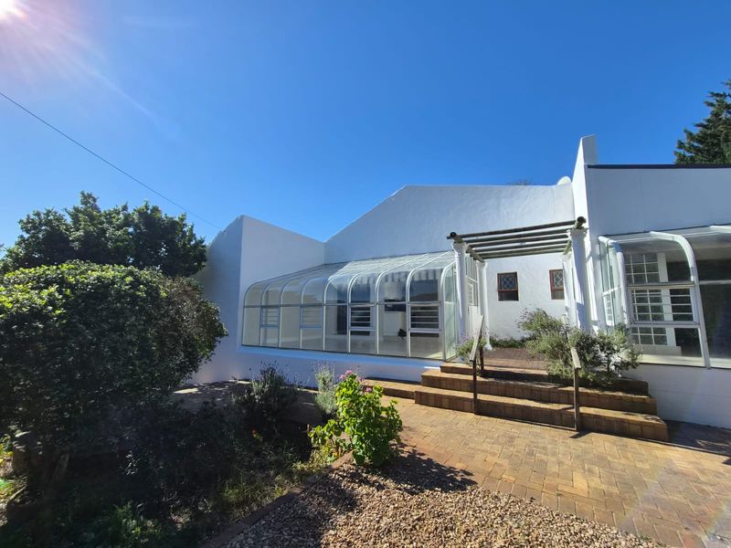 Rear view of the property featuring a glass conservatory, brick paved patio area, and a timber pergola leading to the garden.