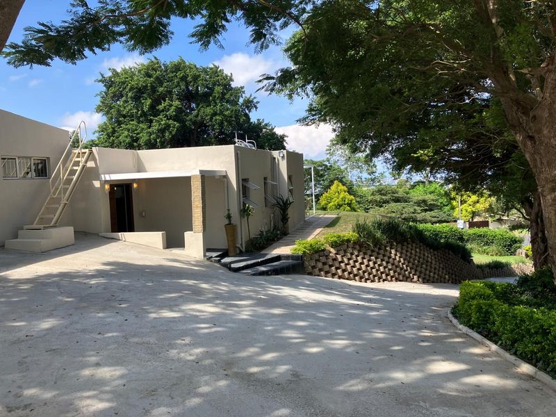 Front exterior view of the property featuring a concrete driveway, external staircase, and landscaped retaining wall area.