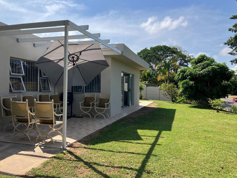 A covered patio area featuring a white pergola structure, tiled flooring, and direct access to the garden through sliding glass doors.