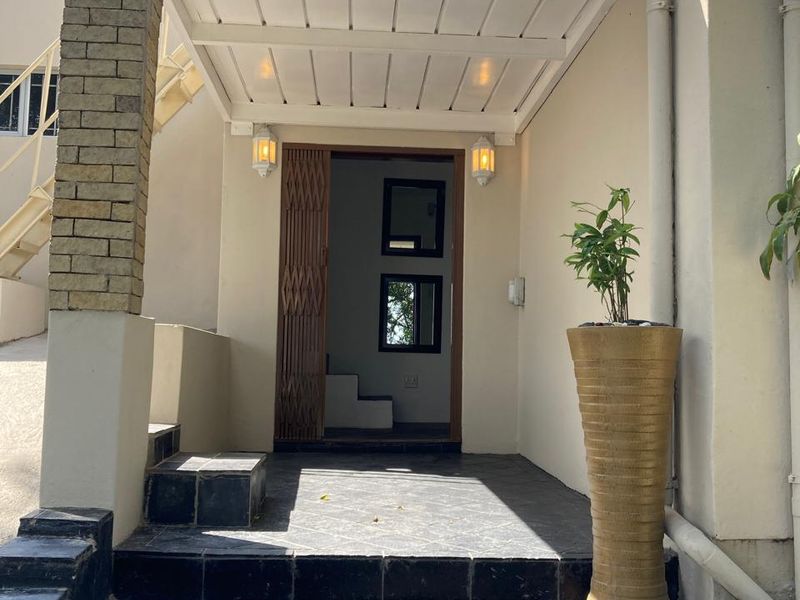 A well-maintained front entrance featuring a covered patio area with stone-clad detailing, tiled flooring, and secure access.