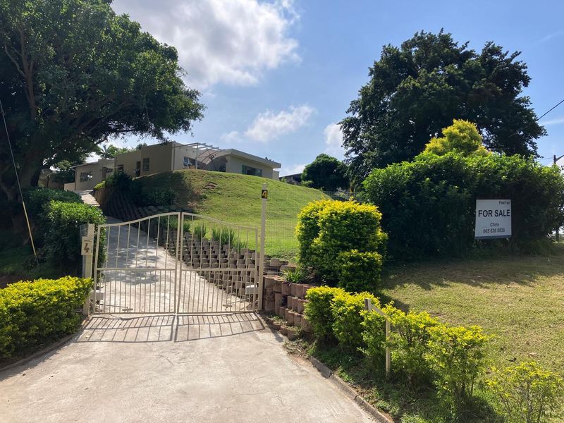 Front view of the property featuring a concrete driveway, secure metal gate, and elevated garden area with retaining walls.