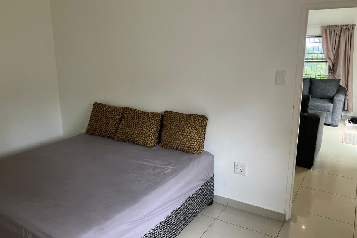A simple bedroom featuring tiled flooring and neutral walls, with a doorway leading to an adjacent living area.