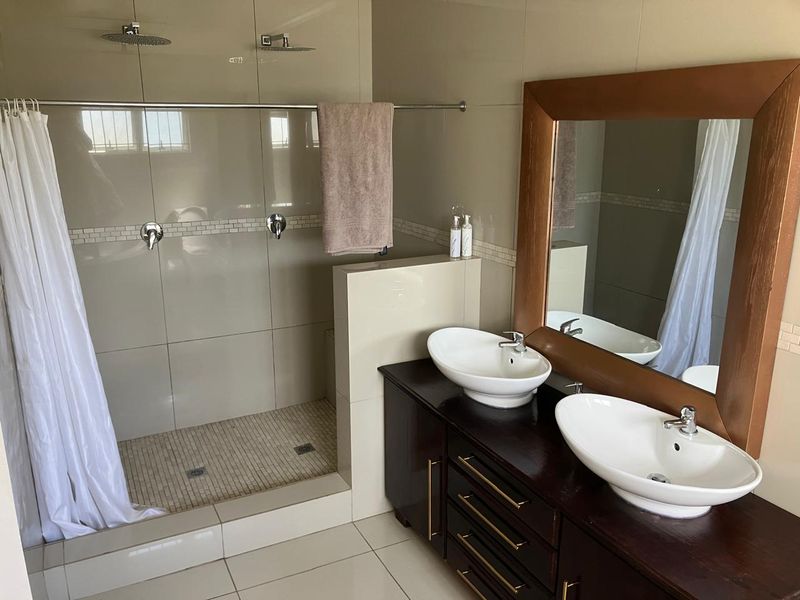 Modern bathroom featuring a spacious walk-in shower with dual shower heads and a double vanity with vessel sinks and a large wooden-framed mirror.