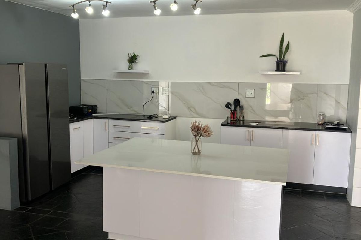 Modern kitchen featuring white cabinetry, dark stone countertops, a central island, marble-look splashback, and contemporary track lighting.