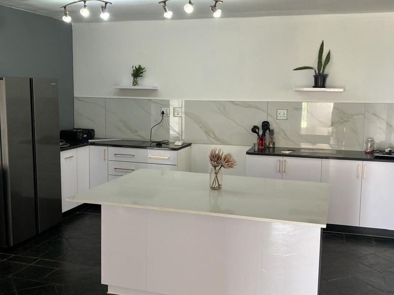 Modern kitchen featuring white cabinetry, dark stone countertops, a central island, marble-look splashback, and contemporary track lighting.