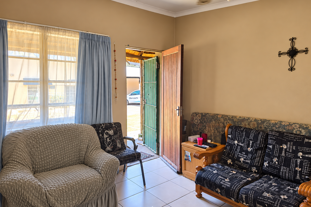 A living room area featuring tiled flooring, a ceiling fan, and direct access to the exterior through a timber door with a security gate.