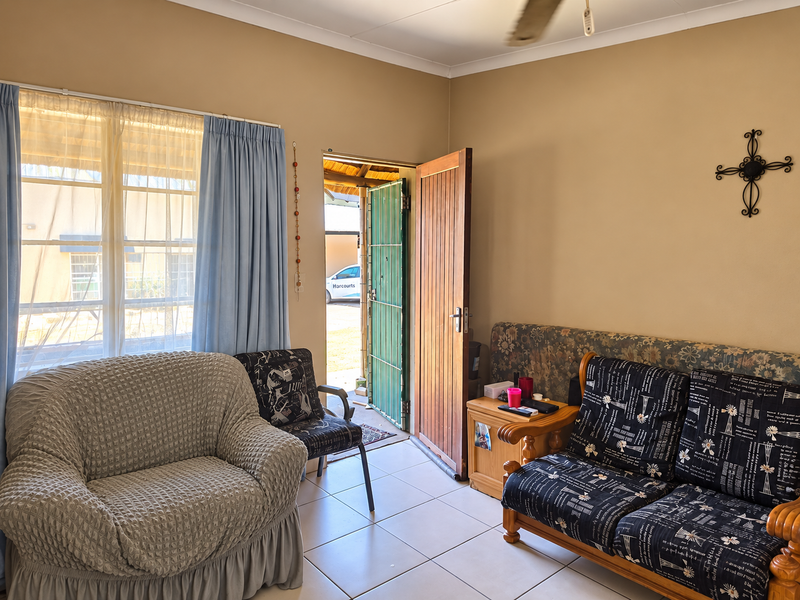 A living room area featuring tiled flooring, a ceiling fan, and direct access to the exterior through a timber door with a security gate.