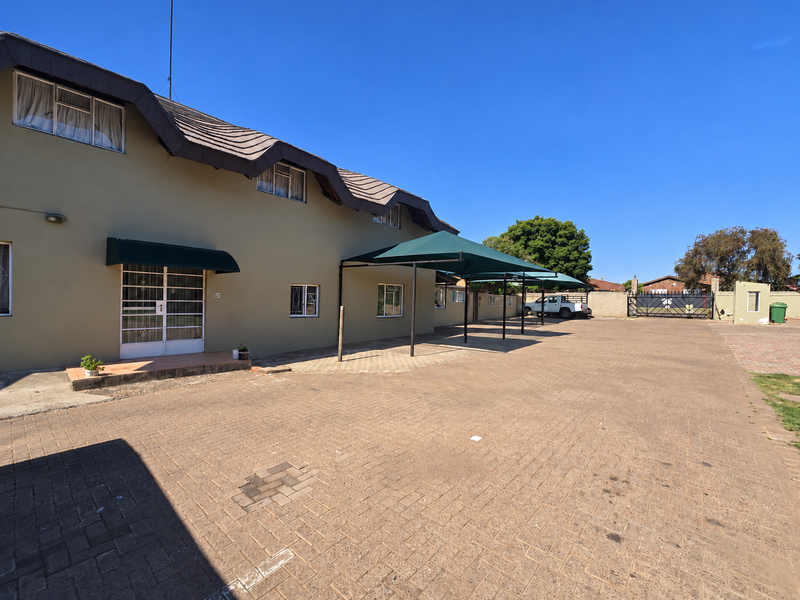 Exterior view of a retirement village building featuring a paved driveway, covered parking bays, and secure access points.
