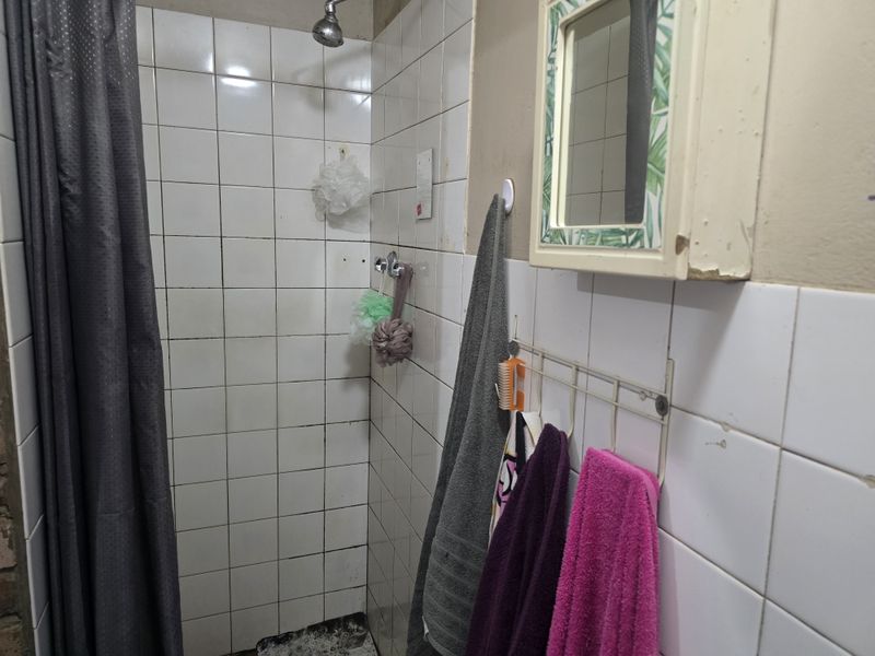 A functional bathroom shower area featuring white wall tiles, a fixed shower head, and a wall-mounted medicine cabinet.